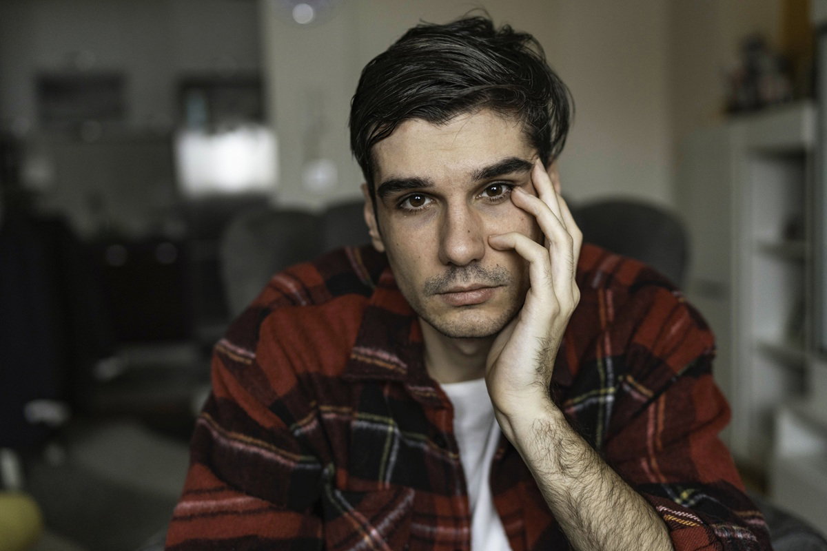 mężczyzna w wieku około 30 lat z wyraźnymi brwiami w kraciastej koszuli siedzi zatroskany