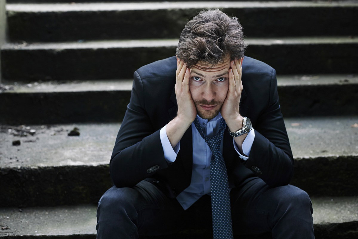 mężczyzna w wieku 35 plus w garniturze siedzi na schodach załamany