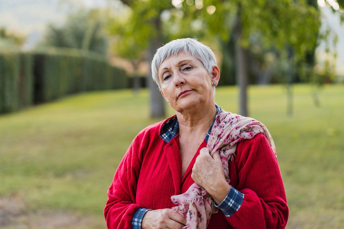 kobieta w wieku 60 plus z krótkimi włosami w czerwonej bluzie ze zblazowanym wyrazem twarzy