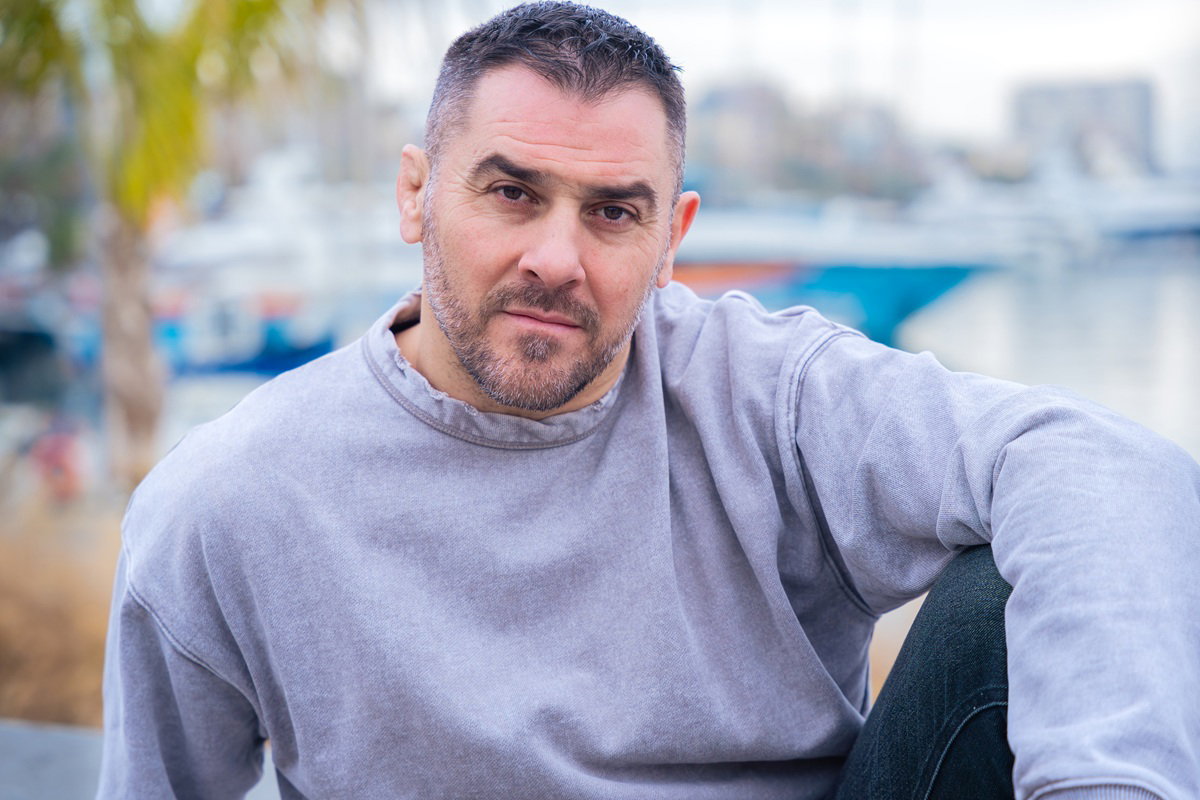 mężczyzna w wieku 40 plus z zarostem w szarej bluzie siedzi na zewnątrz zasępiony
