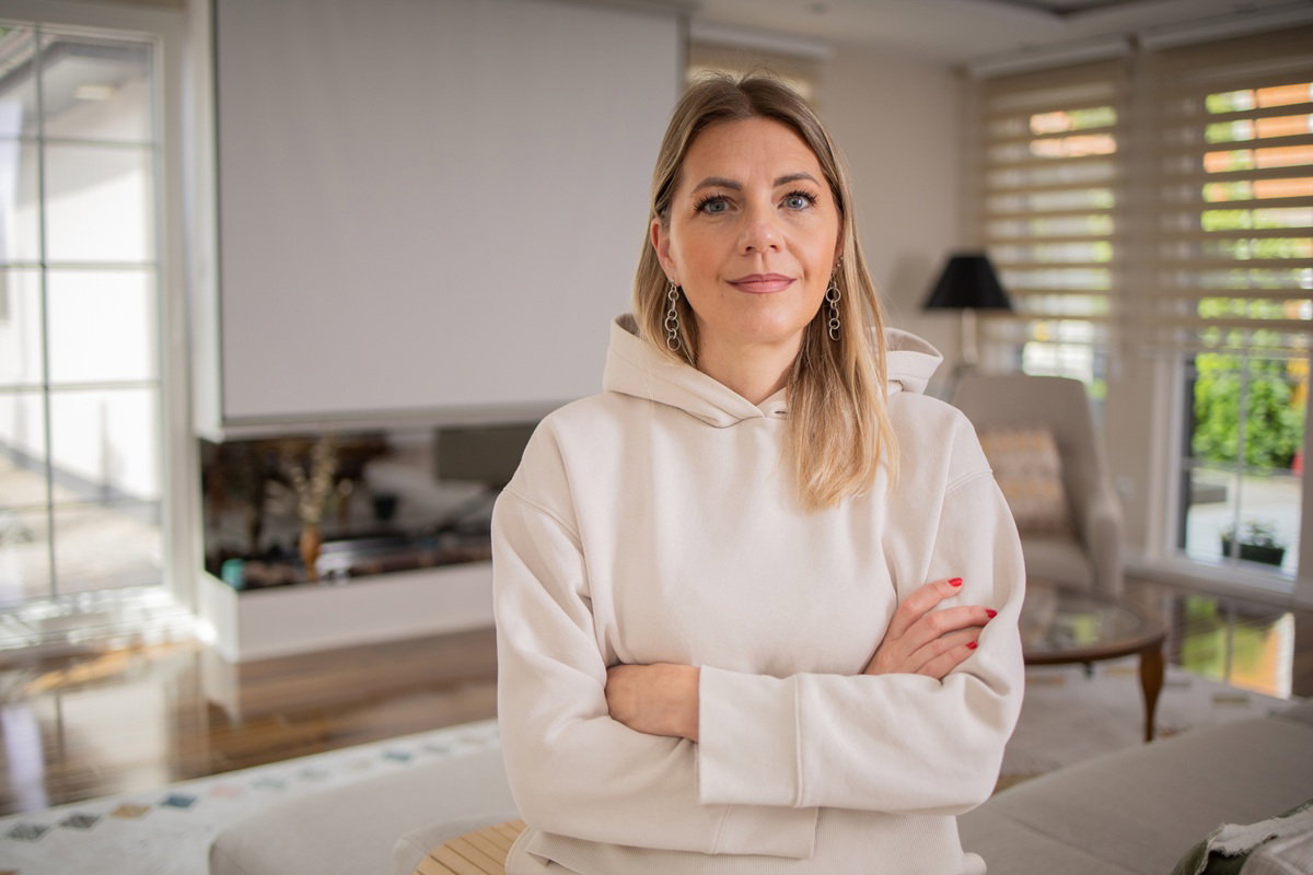 kobieta w wieku około 40 lat w jasnej bluzie z kapturem stoi w salonie poddenerwowana