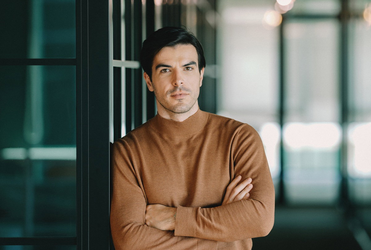 przystojny mężczyzna w wieku 30 plus z ciemnymi włosami w swetrze w kolorze camel i poważnym wyrazem twarzy