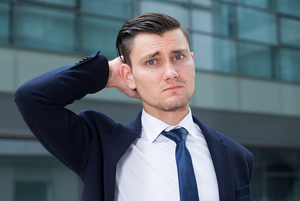 mężczyzna w wieku 30 plus w garniturze i pod krawatem zmartwiony stoi na tle oszklonego budynku
