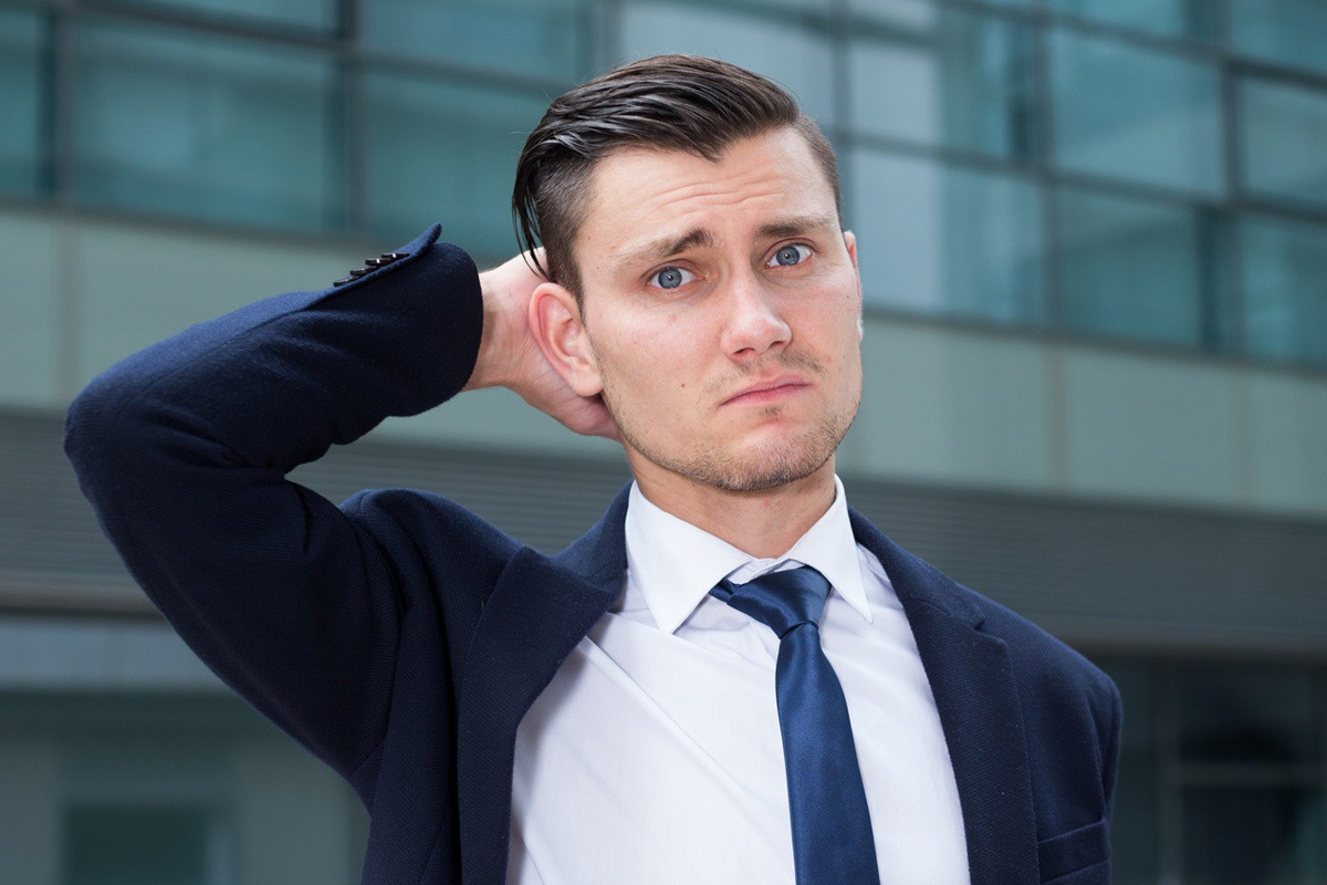 mężczyzna w wieku 30 plus w garniturze i pod krawatem zmartwiony stoi na tle oszklonego budynku