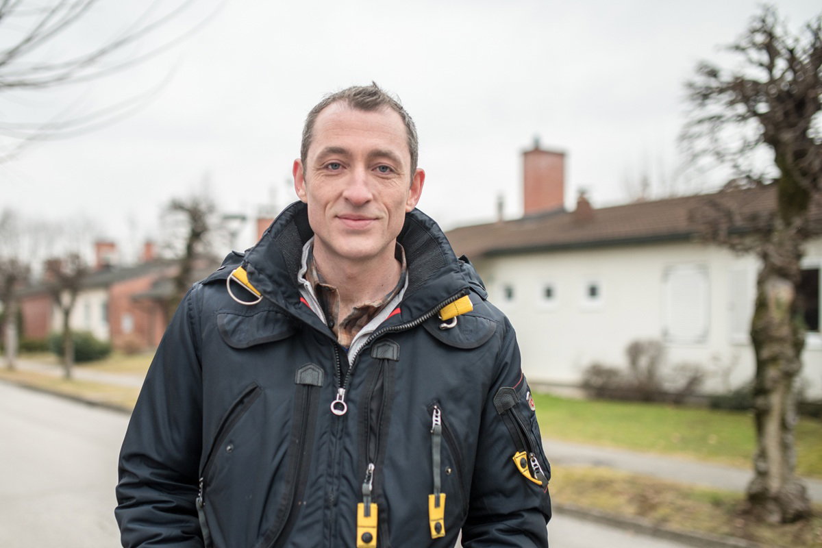 mężczyzna w wieku 40 plus w czarnej kurtce stoi na zewnątrz i kpiąco się uśmiecha