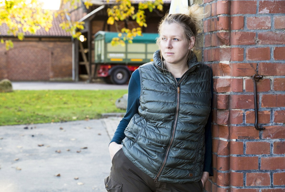 kobieta w wieku około 25 lat blondynka w zielonym bezrękawniku opiera się o mur zamyślona