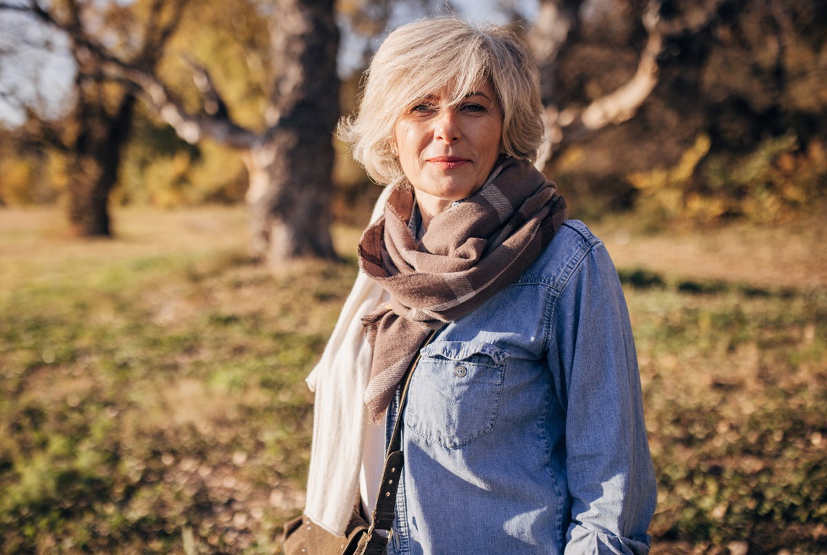 kobieta w wieku 50 plus z chustą na szyi na jesiennym spacerze stoi zamyślona i poważna