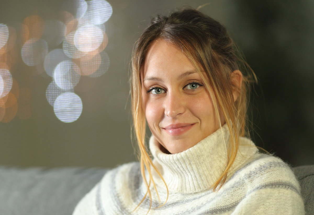 kobieta w wieku 30 plus ciemna blondynka w białym swetrze z golfem patrzy pobłażliwie przed siebie