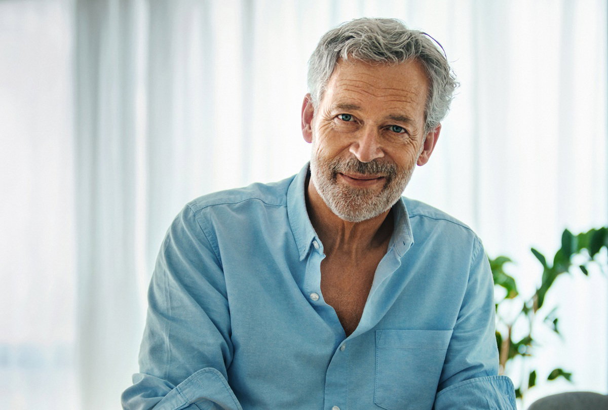 przystojny mężczyzna w wieku 60 plus w jasnej koszuli siedzi w salonie i lekko się uśmiecha
