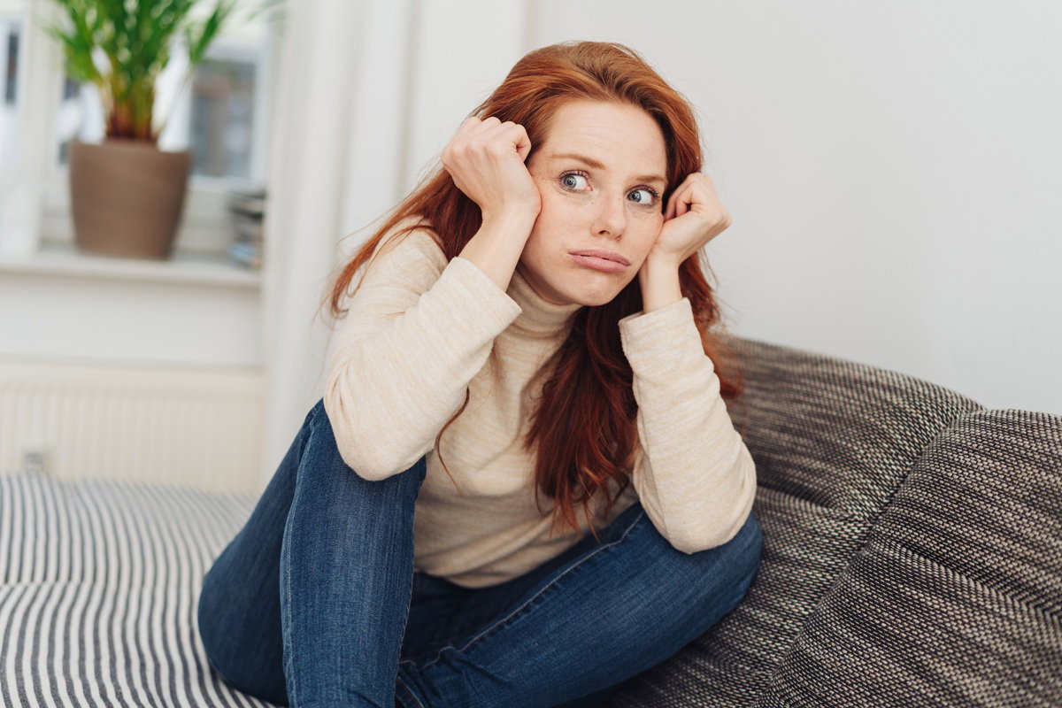 młoda kobieta w wieku 20 plus z rudymi długimi włosami siedzi na kanapie zdziwiona i zdegustowana