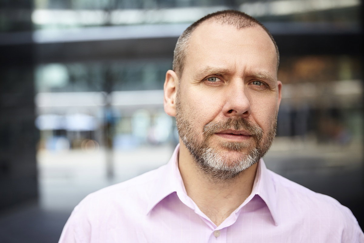 mężczyzna w wieku 40 plus z zarostem łysiejący w różowej koszuli stoi zamyślony i smutny