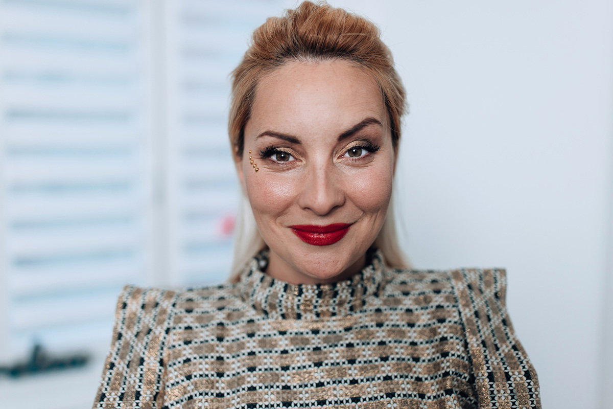 kobieta w wieku około 35 plus w pełnym makijażu stoi wewnątrz i uśmiecha się zalotnie