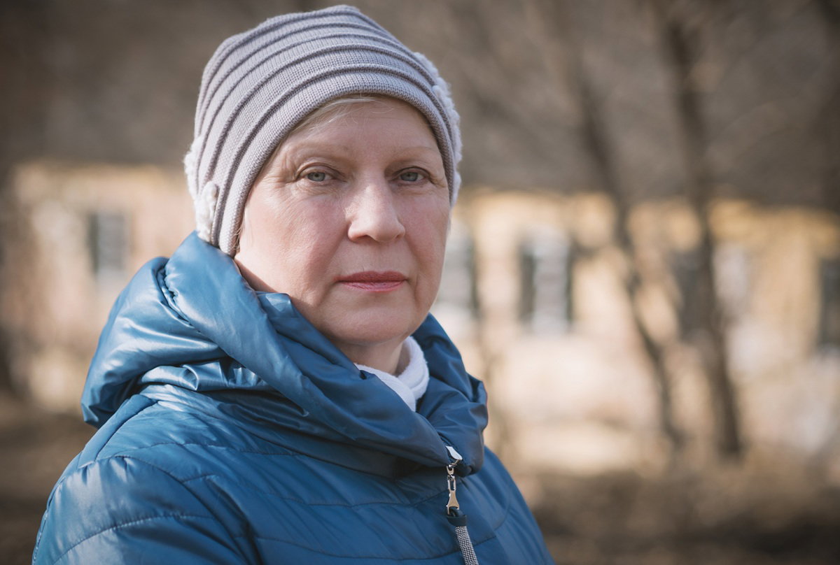 kobieta w wieku około 60 lat w czapce i kurtce stoi na zewnątrz zamyślona