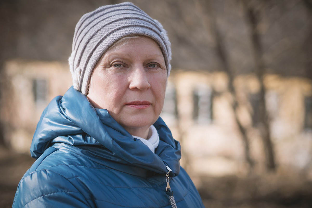 kobieta w wieku około 60 lat w czapce i kurtce stoi na zewnątrz zamyślona