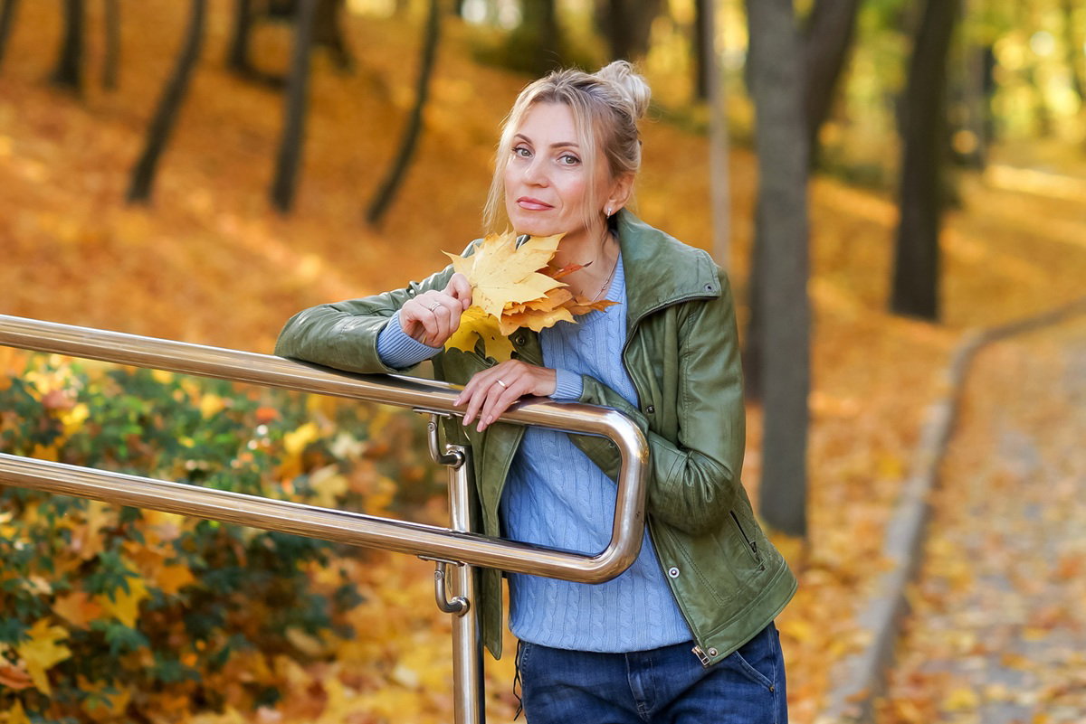 kobieta w wieku 40 plus na spacerze w jesiennym parku z bukietem liści zamyślona