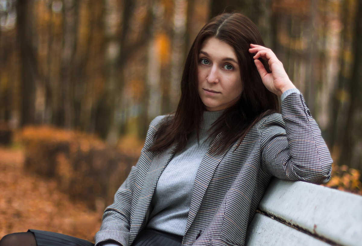 kobieta w wieku 30 plus w skromnym stroju siedzi na ławce w jesiennym parku smutna i zamyślona