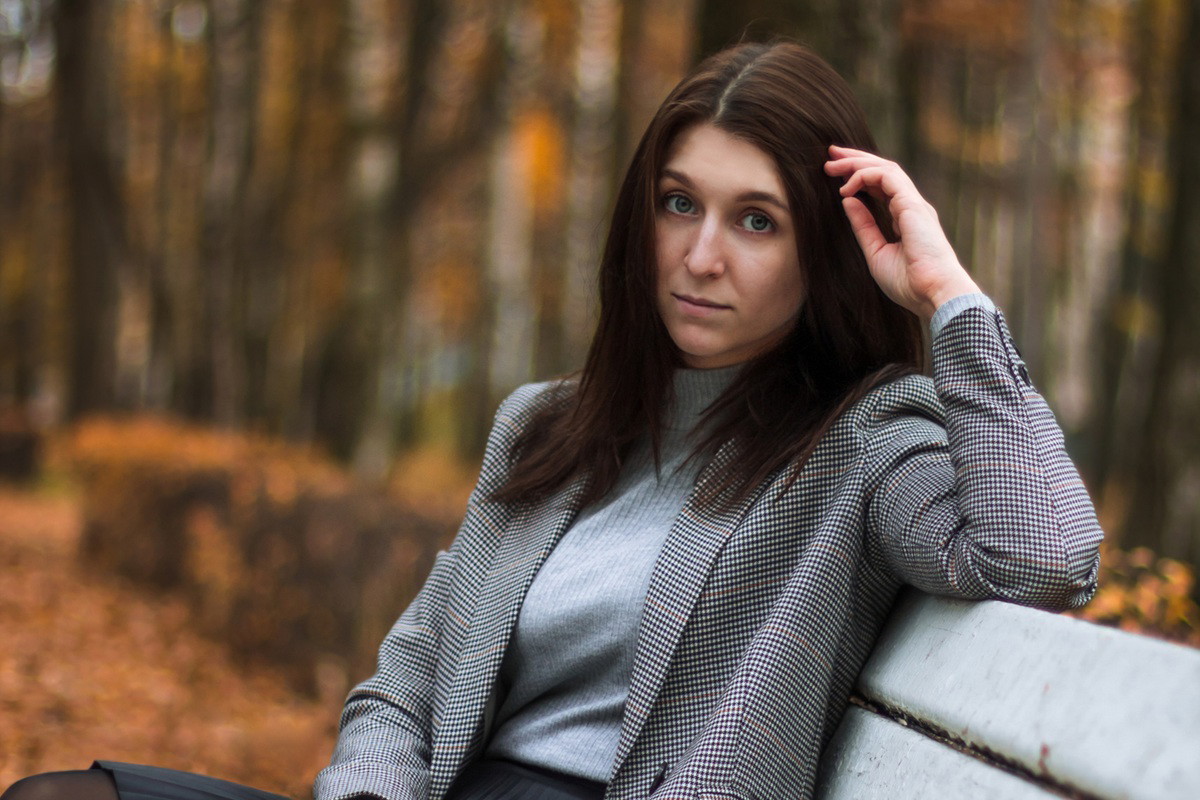 kobieta w wieku 30 plus w skromnym stroju siedzi na ławce w jesiennym parku smutna i zamyślona