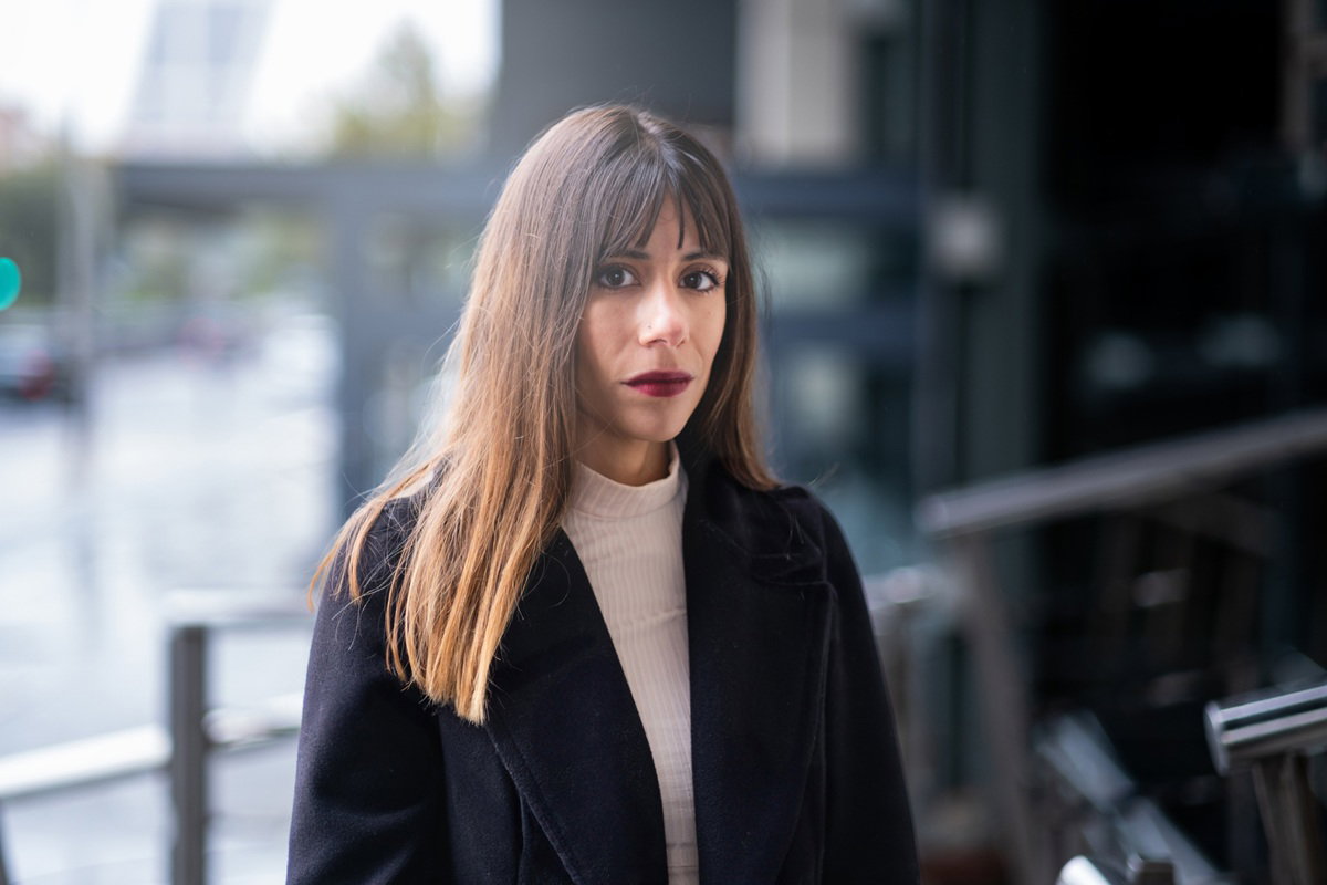 kobieta w wieku 30 plus stoi zmartwiona i zamyślona w ciemnym płaszczu i z ciemnoczerwoną szminką na ustach