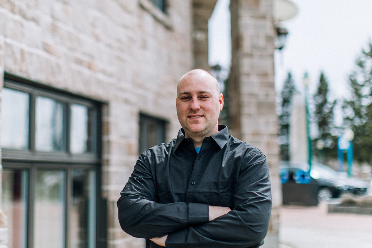 mężczyzna w wieku 40 plus łysy stoi na tle kamiennego budynku z oknami lekko zakłopotany