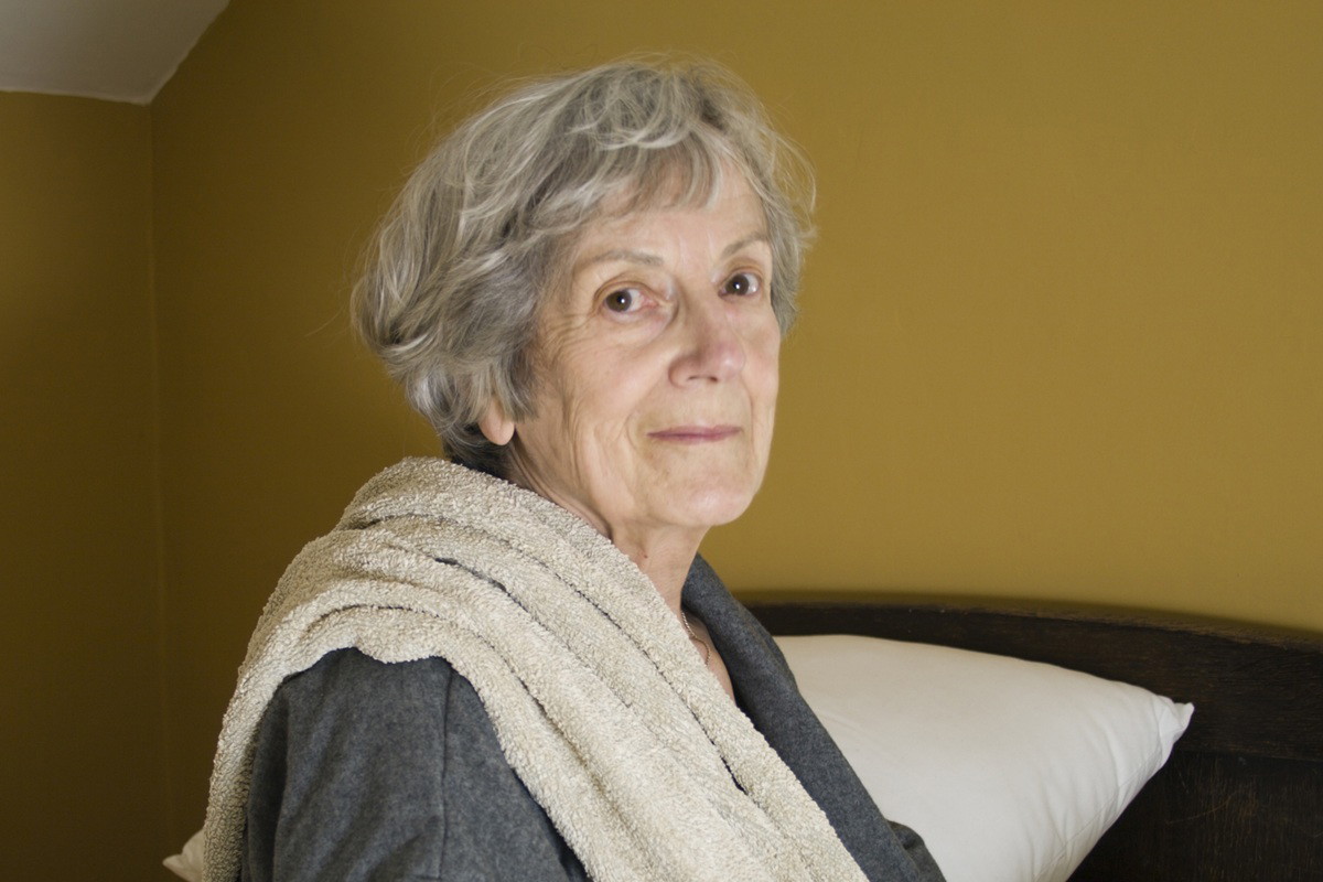 kobieta w wieku 75 plus siedzi z ręcznikiem na ramieniu smutna i zamyślona