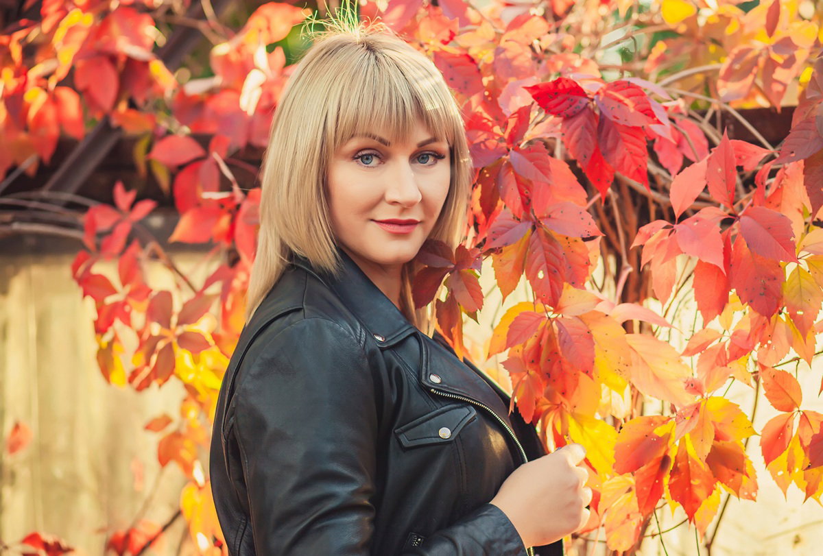 kobieta w wieku 30 plus blondynka w skórzanej kurtce stoi na tle jesiennych liści zamyślona