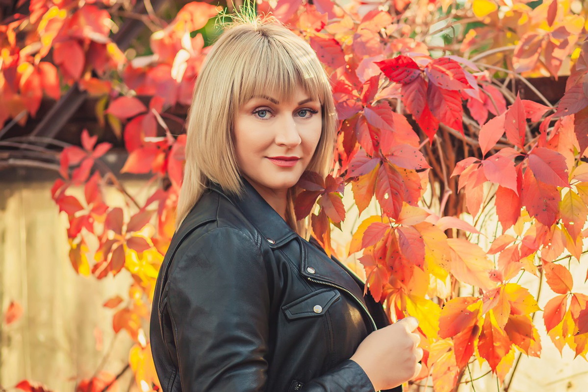 kobieta w wieku 30 plus blondynka w skórzanej kurtce stoi na tle jesiennych liści zamyślona