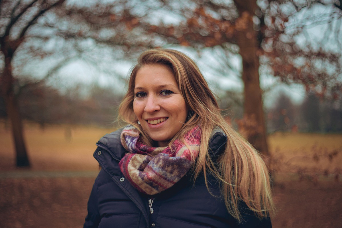 kobieta w wieku 30 plus blondynka w kurtce i szalu stoi na zewnątrz i się uśmiecha
