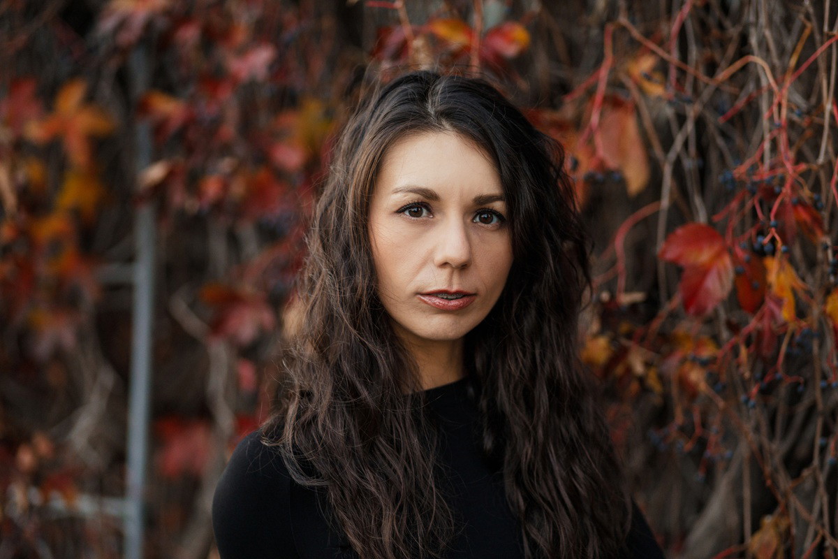 kobieta w wieku 30 plus z długimi ciemnymi włosami stoi na tle winorośli zamyślona i smutna