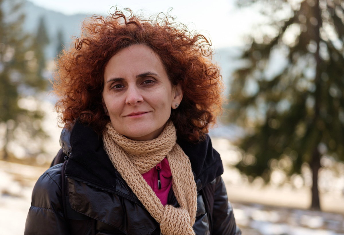 kobieta w wieku 50 plus z burzą rudych loków z szaliczkiem patrzy zamyślona w dal