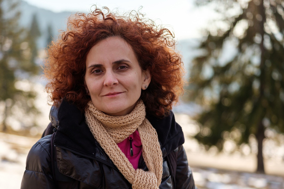 kobieta w wieku 50 plus z burzą rudych loków z szaliczkiem patrzy zamyślona w dal