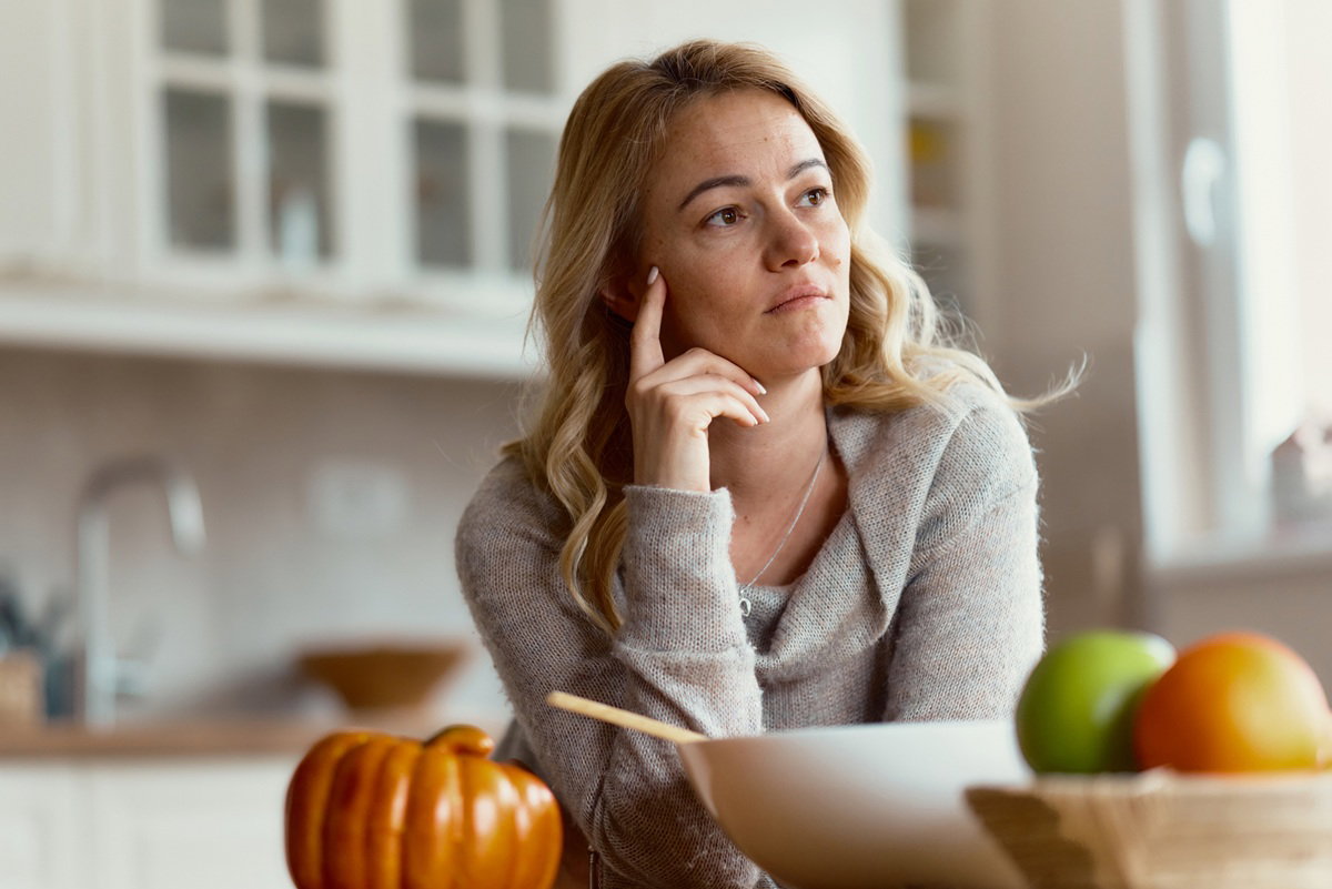 kobieta w wieku 40 plus siedzi w kuchni zamyślona przy stole z owocami