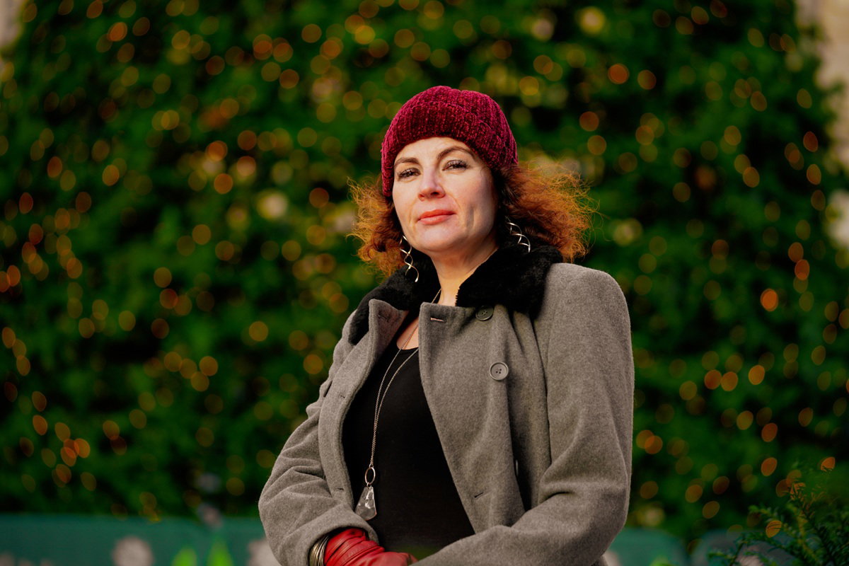 kobieta w wieku 45 plus w szarym płaszczu i czapce stoi na zewnątrz z niepewnym wyrazem twarzy