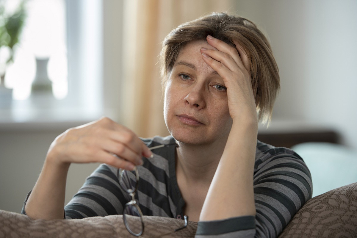 kobieta w wieku 40 plus siedzi na kanapie załamana z okularami w ręku i rozmyśla