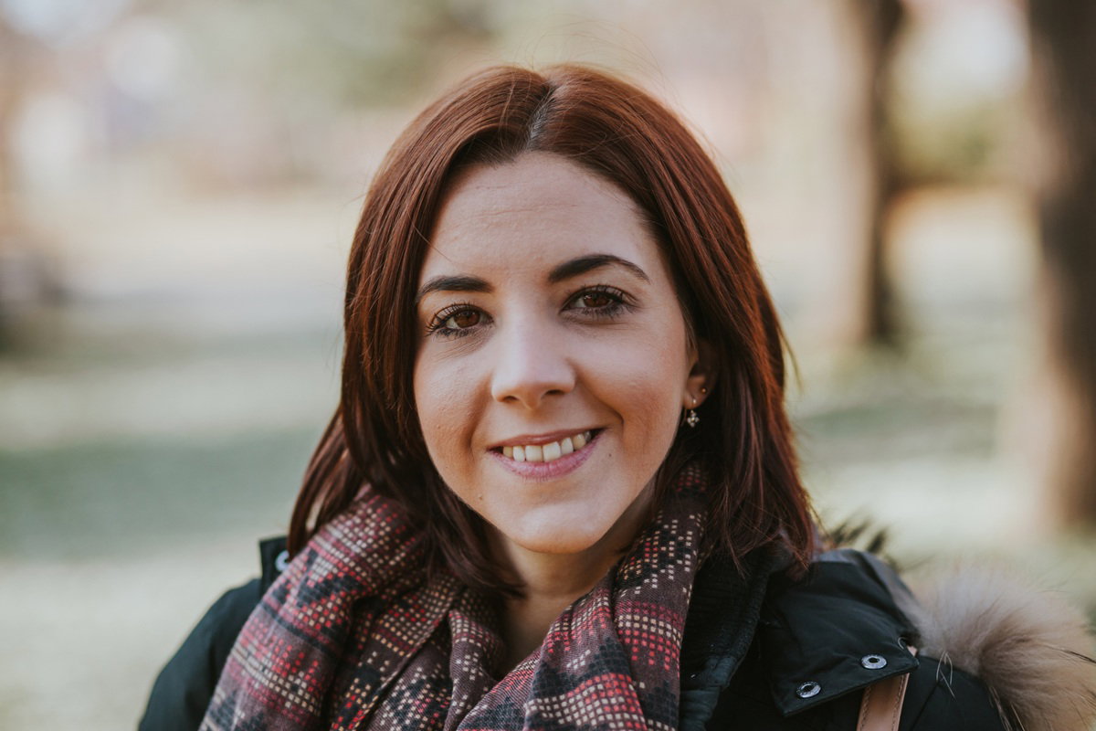 kobieta w wieku 25 plus z brązowymi oczami i ze wzorzystym szalem na szyi uśmiecha się stojąc na dworze