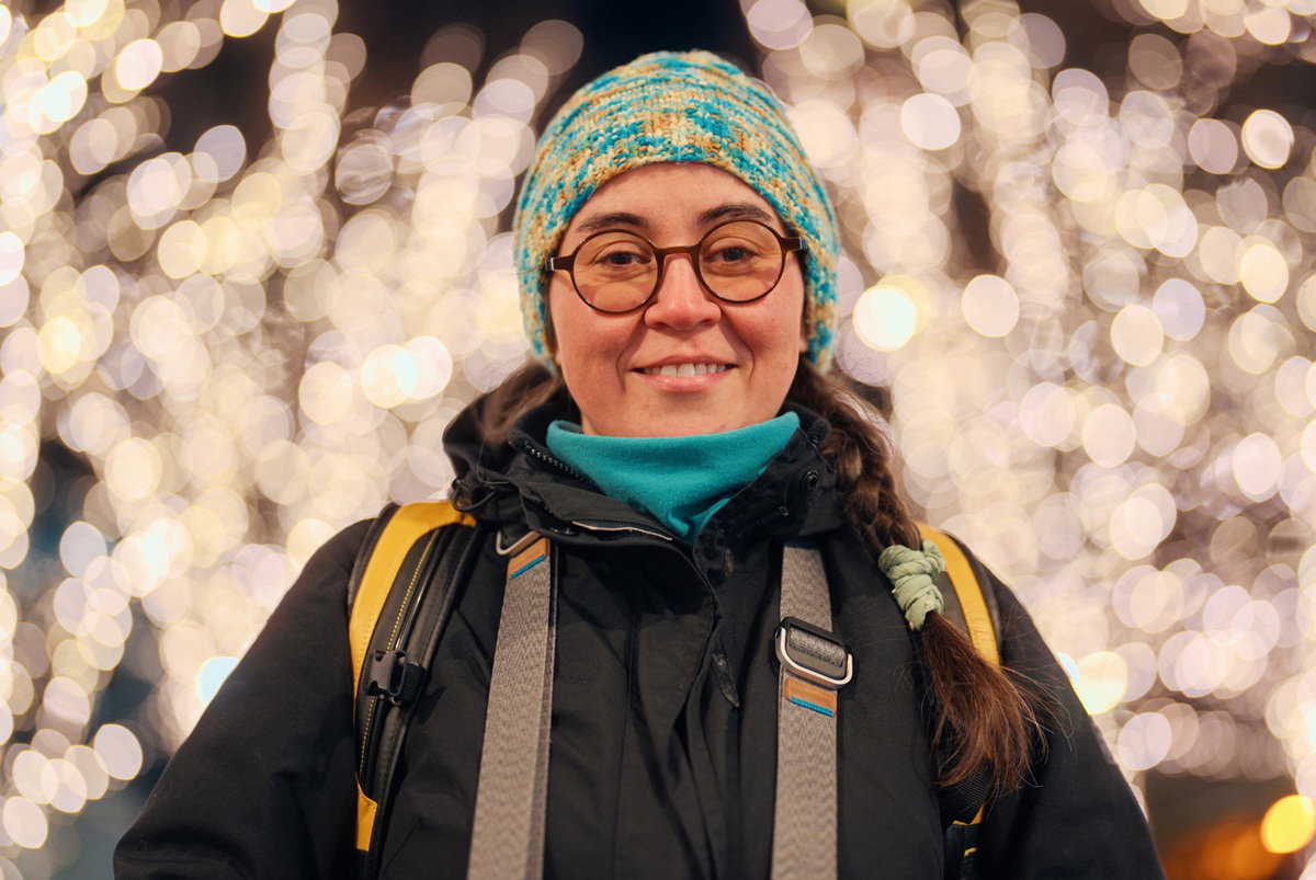 kobieta w czapce i w okularach w wieku około 40 lat stoi na tle świetlnych dekoracji i się uśmiecha