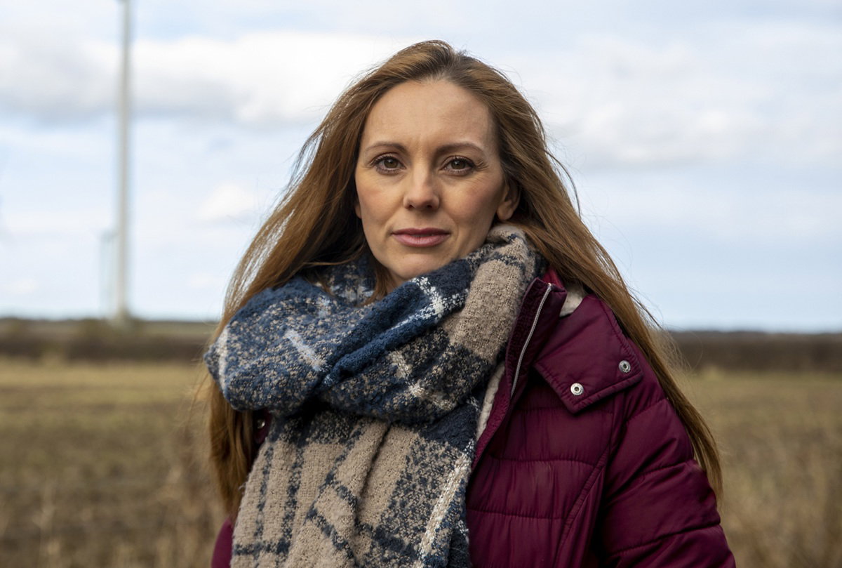 kobieta w wieku 35 plus w kraciastym szalu i bordowej kurtce stoi na polu smutna i zamyślona