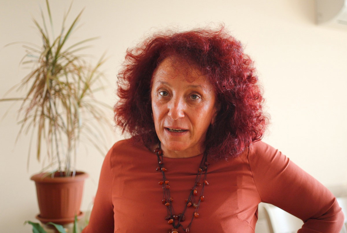 kobieta w wieku 50 plus w pomarańczowej bluzce z rudymi lokami stoi wkurzona w salonie