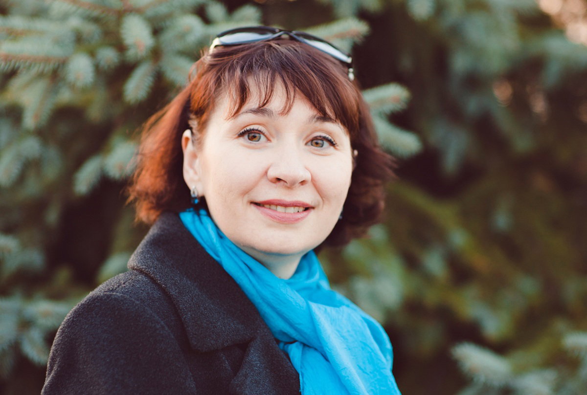 kobieta w wieku prawie 40 lat z niebieskim szalikiem na szyi stoi na zewnątrz pełna nadziei