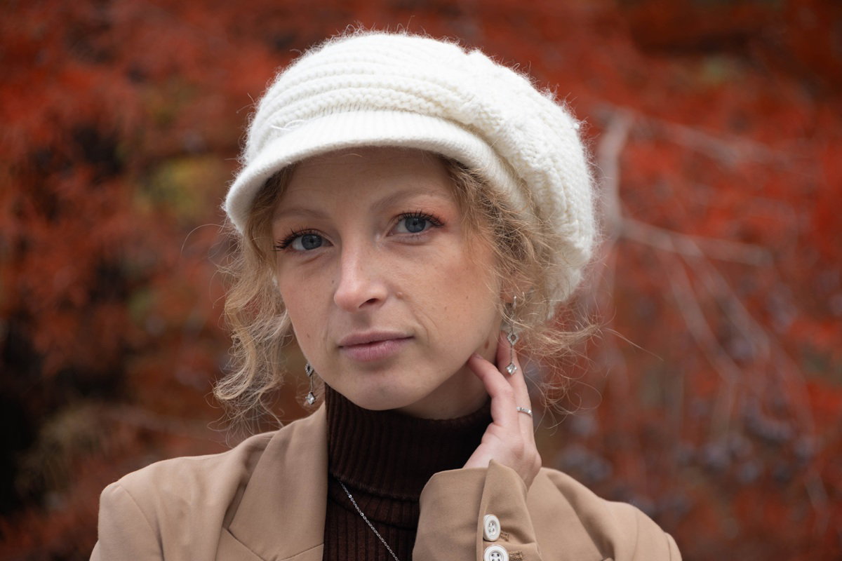 kobieta w białej czapce z daszkiem typu kaszkiet blondynka w wieku 30 plus stoi zamyślona na tle jesiennych drzew