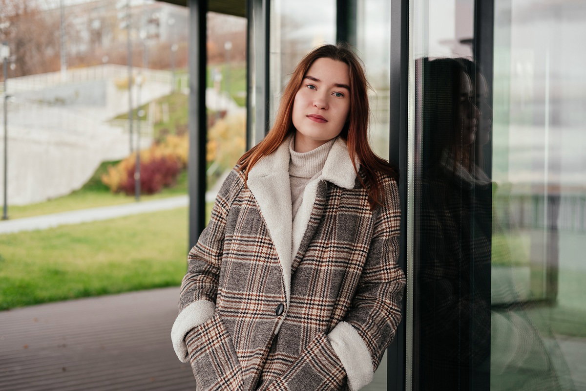 młoda dziewczyna 20 plus w kraciastym płaszczu stoi zamyślona na tle szklanego budynku
