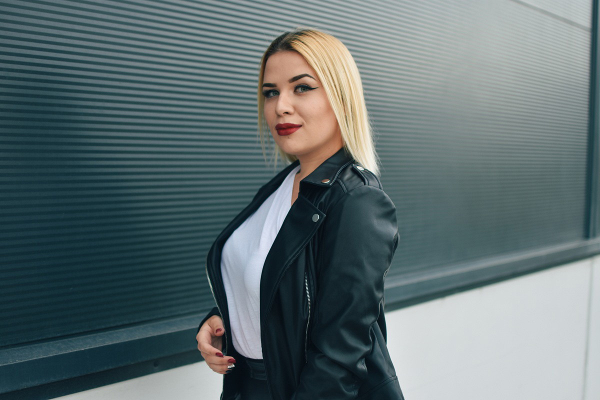 kobieta w wieku 30 plus blondynka w ramonesce stoi z zawadiackim uśmiechem