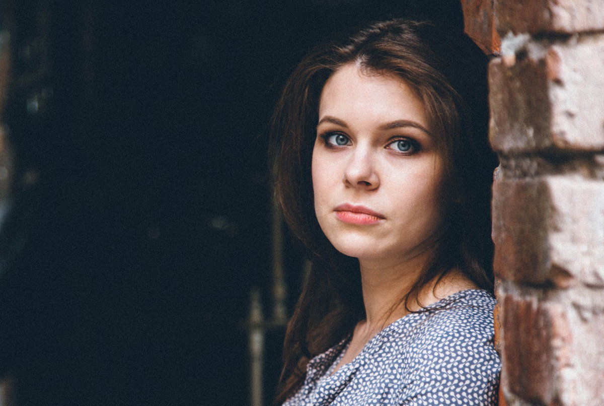 kobieta w wieku 30 plus stoi przy ceglanej ścianie zamyślona i smutna