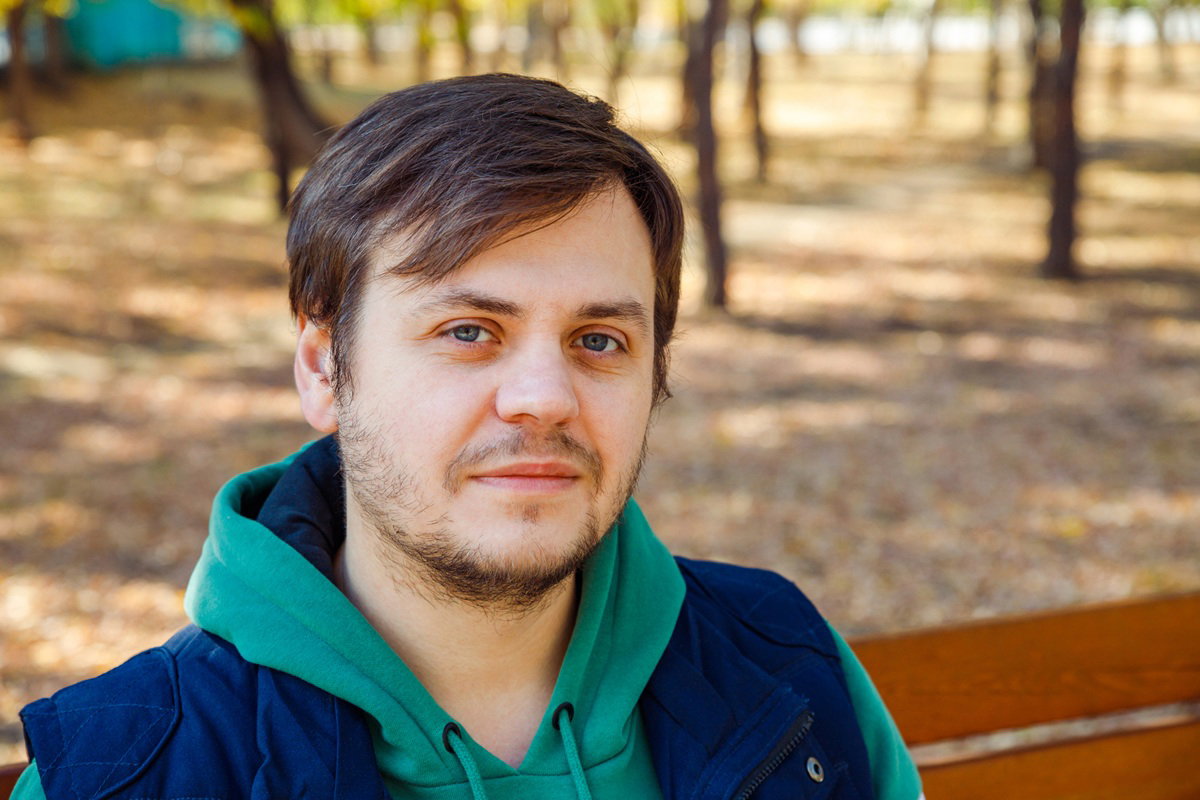 mężczyzna w wieku 30 plus w zielonej bluzie z kapturem i bezrękawniku siedzi na ławce zawiedziony i zamyślony