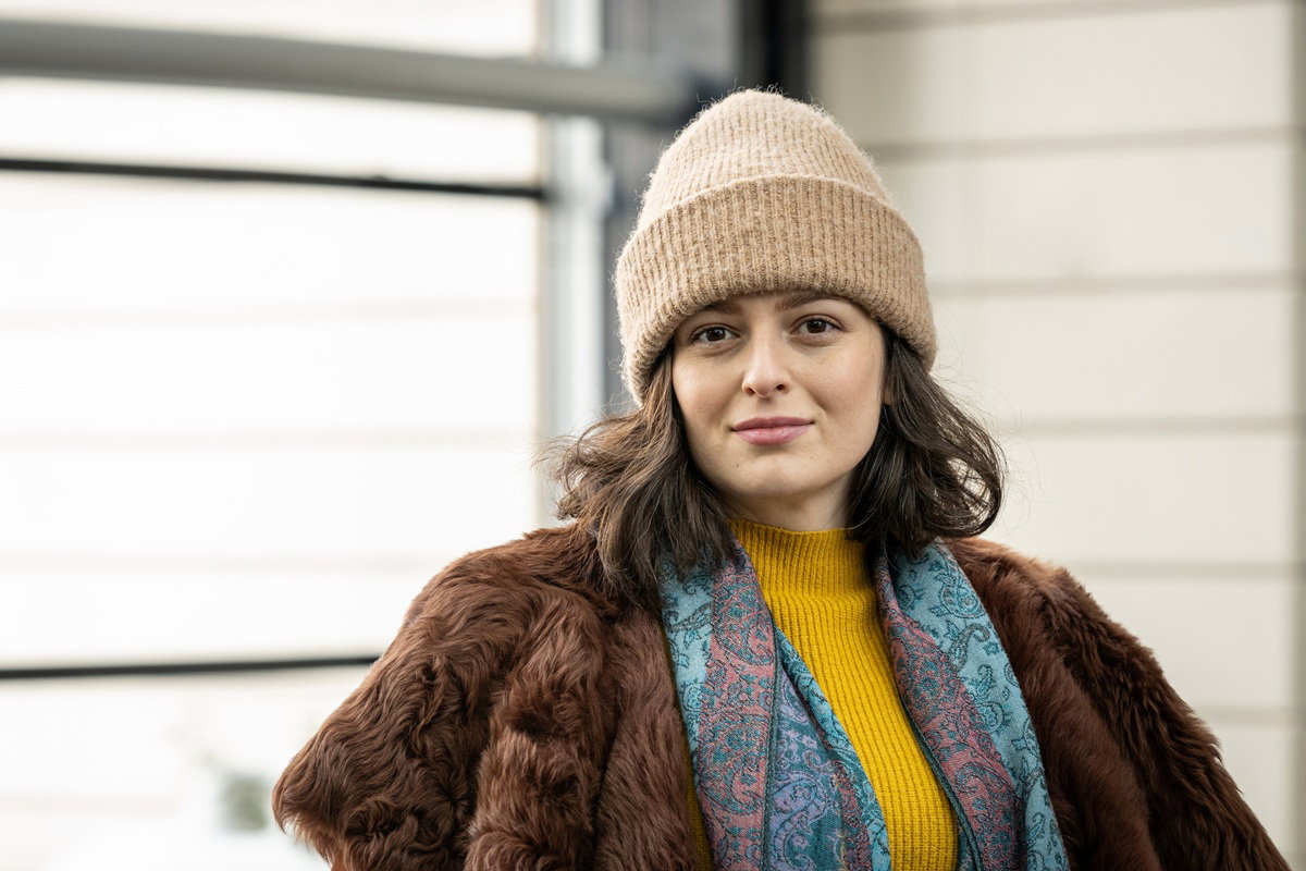 kobieta w wieku 35 plus w czapce beżowej i futrze stoi dumna i zadowolona na tle budynku