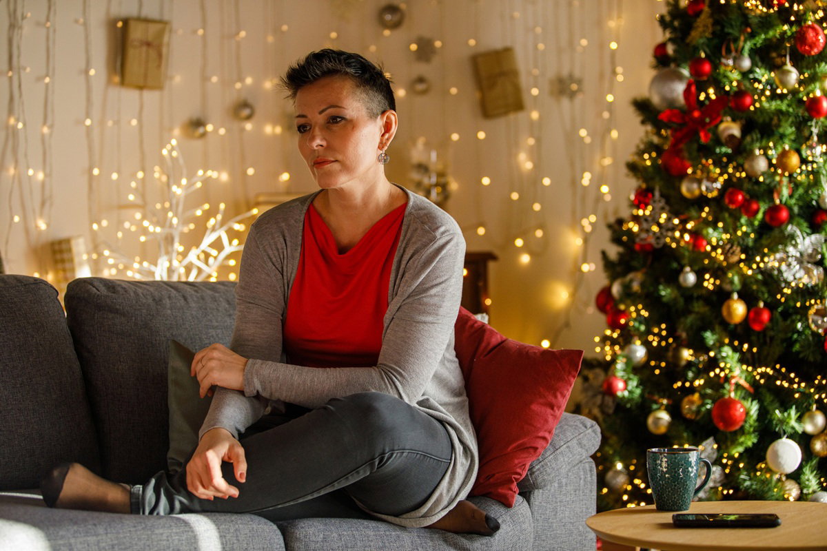 kobieta w wieku około 40 lat z krótkimi czarnymi włosami siedzi przy choince smutna