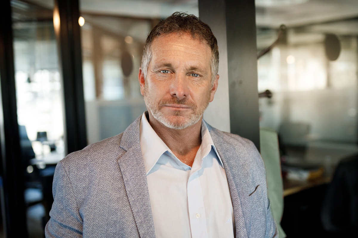 mężczyzna w wieku 45 plus w marynarce i rozpiętej pod szyją koszuli stoi zamyślony w biurze