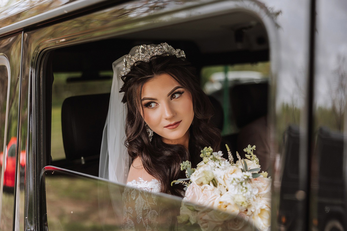 panna młoda siedzi w samochodzie z bukietem ślubnym i patrzy zamyślona i smutna w dal