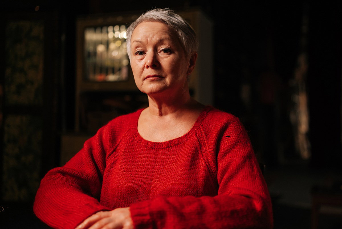 kobieta w wieku 65 plus w czerwonym swetrze zasmucona i zamyślona w ciemny pomieszczeniu