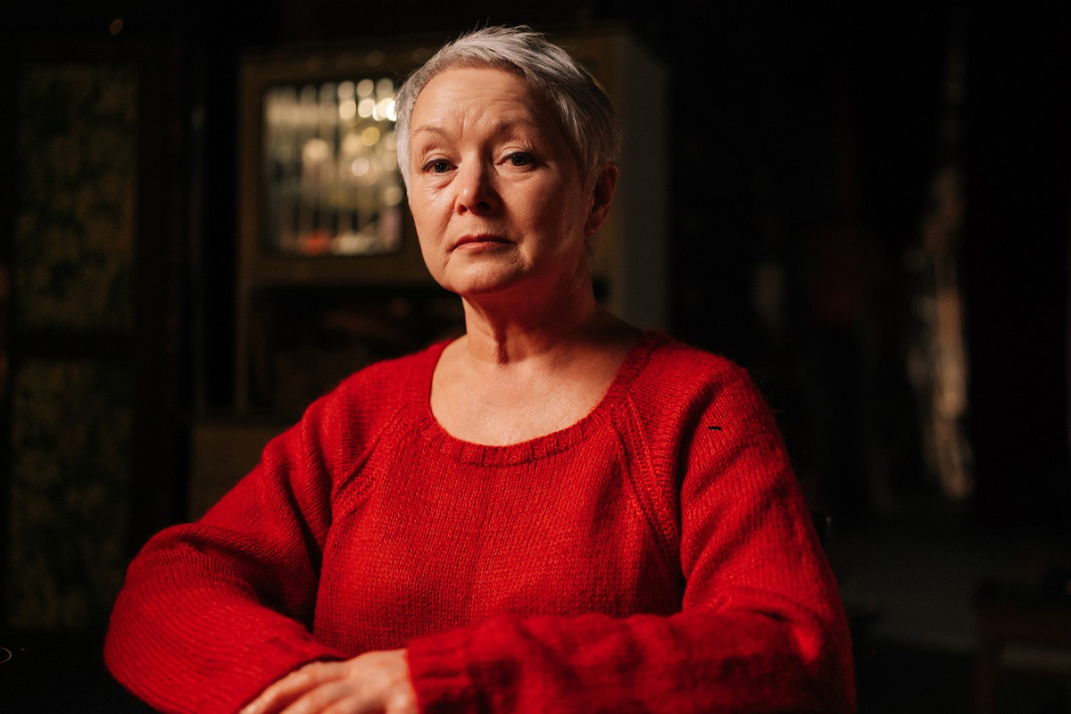 kobieta w wieku 65 plus w czerwonym swetrze zasmucona i zamyślona w ciemny pomieszczeniu