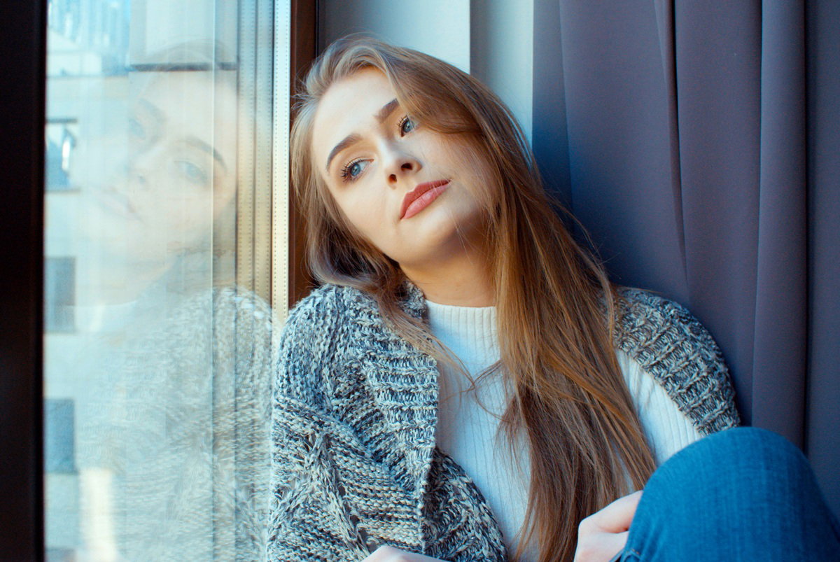 dziewczyna w wieku 25 plus blondynka w melanżowym swetrze siedzi przy oknie zamyślona